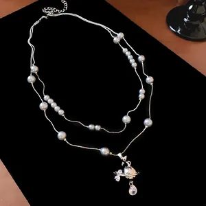 Detail view of a double-layered grey pearl necklace with a rhinestone Saturn pendant.