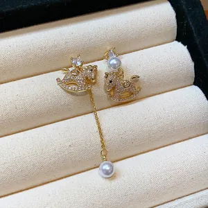 Detail view of gold-plated rocking horse earrings with zircon and pearl tassels