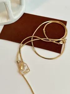 Close-up of gold-plated snake chain necklace with gold leaf geometric pendant.