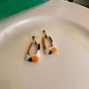 Macro view of geometric hollow earrings featuring vibrant orange and green enamel color blocking