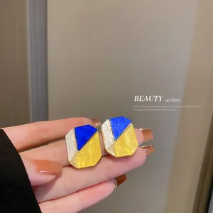 Close-up detail of geometric asymmetric earrings featuring blue and yellow enamel finish