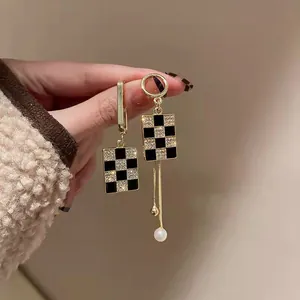 Close-up of asymmetric gold earrings with black white checkerboard and pearl drop