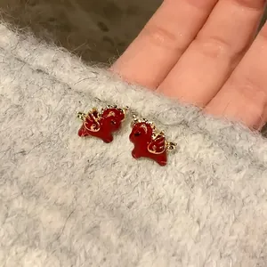 Detailed macro view of cute red enamel unicorn stud earrings with gold wings on grey knit fabric