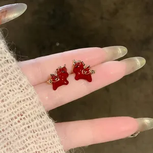 Close-up view of minimalist red enamel winged horse stud earrings held on a hand