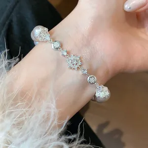 Detailed view of an elegant pearl bracelet featuring sparkling zircon flowers on a wrist.
