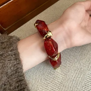 Detail shot of a red acrylic beaded bracelet with golden accents worn on a wrist