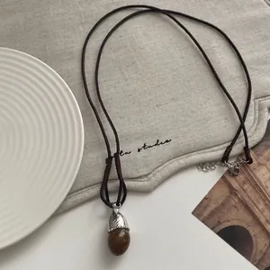 Detailed shot of a vintage acorn pendant necklace featuring a dark brown cord and resin stone