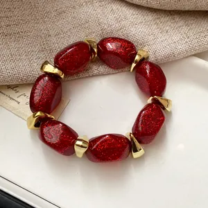 Close-up of elegant red glittery acrylic oval beaded bracelet with gold metal spacers.