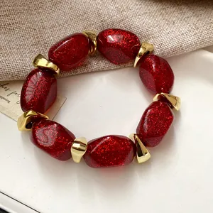 Close-up detail of a fashion bracelet featuring red glittery oval acrylic beads and gold spacers