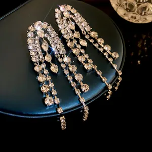 Elegant long silver needle earrings with shimmering rhinestone tassels on a jewelry box