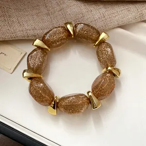 Detailed macro view of an amber glitter acrylic oval beaded bracelet with gold accents.