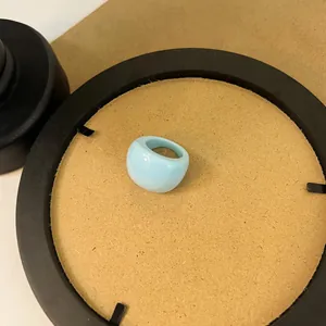 Macro detail shot of a smooth light blue chunky resin ring displayed on a tan circular base