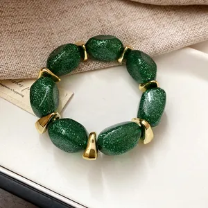 Close-up of green glitter acrylic oval beaded bracelet with gold spacers on white tray.
