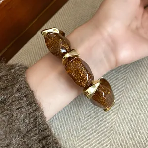 Detailed view of an acrylic oval beaded bracelet with glittery amber stones and gold accents.