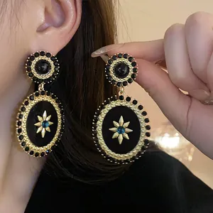 Close-up detail of vintage palace style oval drop earrings in black and gold finish.