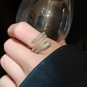 Close-up of elegant gold-plated snake ring with white and green zircons on finger.
