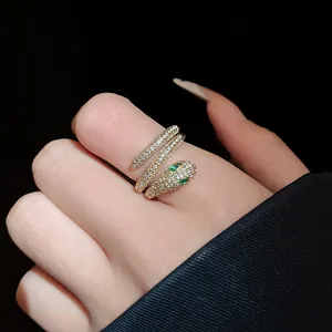 Detailed view of a gold-plated snake ring with pavé zircon and green eyes on finger