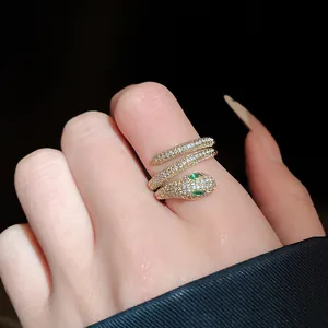 Close-up of a gold-plated snake ring with pavé zircons and green eyes on a finger.