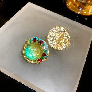 Close-up of vintage palace style asymmetric earrings with green gems and gold texture
