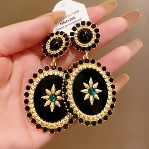Close-up of vintage palace style oval dangle earrings with black stones and gold star motif.