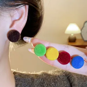 Pendientes de botón redondos con acabado flocado en colores de otoño en una modelo.