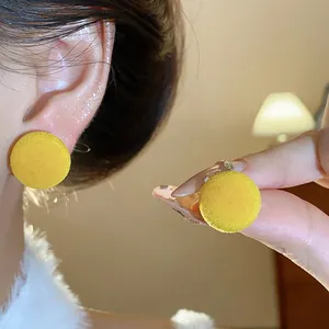 Vista de cerca de pendientes de botón redondos flocados en amarillo brillante en oreja