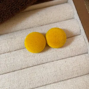 Vista detallada de pendientes redondos de flocado amarillo en un joyero de tela suave.