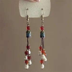Close-up of bohemian tassel earrings with red beads and blue enamel flower caps