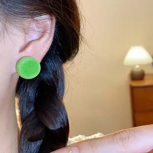 Primer plano de un pendiente de botón redondo flocado verde en una oreja con trenza.