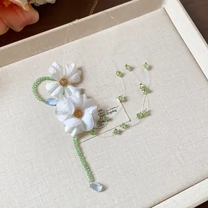 Dettaglio di una collana fatta a mano con fiori di stoffa bianchi e perle di vetro verdi