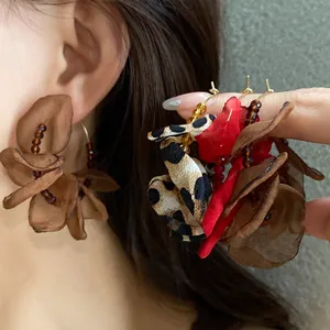 Close-up detail of oversized fabric flower earrings in leopard print and red