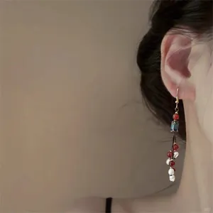 Vintage bohemian drop earrings with red beads and blue enamel floral detail worn on ear