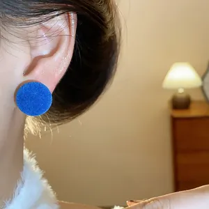 Primer plano de un pendiente redondo flocado azul llevado con luz cálida interior.