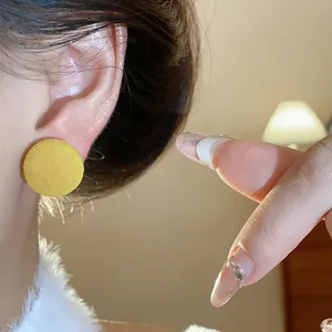 Primer plano que muestra la textura suave de un pendiente redondo flocado amarillo en la oreja