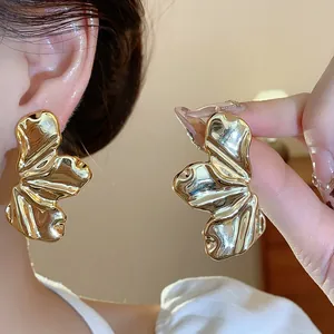 Primer plano de pendientes dorados con textura de hoja y acabado metálico brillante