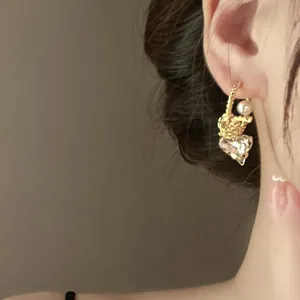 Close-up view of elegant gold C-shape twisted earring featuring a pearl and heart crystal
