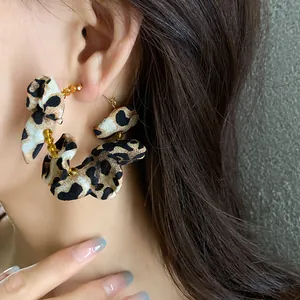 Close-up detail of leopard print fabric hoop earrings with gold beads worn on model