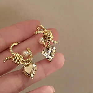 Close-up of golden twisted C-shaped earrings with pearls and heart crystals