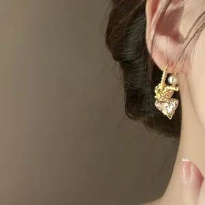 Close-up of golden twisted C-shaped earring with pearl and heart-shaped crystal