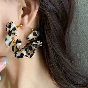 Close-up detail of stylish leopard print fabric hoop earrings with amber beads on ear
