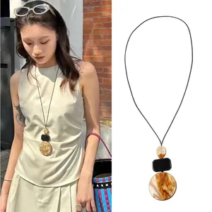 Gros plan d'un long collier bohème avec des pendentifs géométriques en résine marbrée