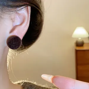 Primer plano de pendientes redondos flocados marrón oscuro usados por una modelo.