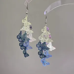 Close-up detail of hollow-out spray-painted butterfly dangle earrings on a clear stand