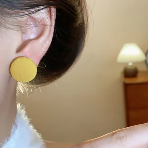 Primer plano detallado de un pendiente de botón redondo amarillo para un look de invierno