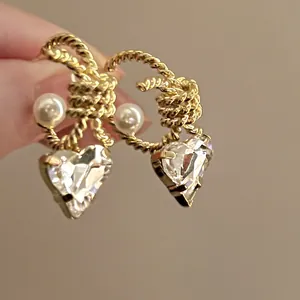 Close-up detail of elegant gold C-shape twisted earrings with pearl and heart crystal charm