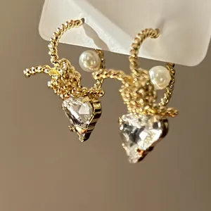 Close-up detail of gold twisted C-shape earrings with heart crystals and white pearls