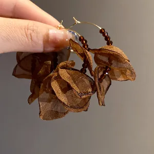 Detailed close-up of brown mesh fabric floral earrings with beaded gold hoops
