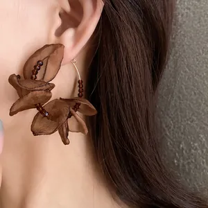 Close-up detail of stylish brown fabric flower hoop earring with beads worn on ear
