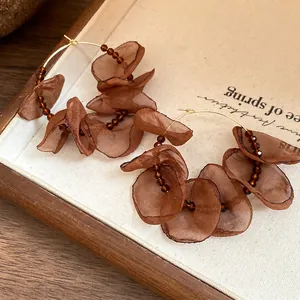 Macro detail of elegant brown fabric flower hoop earrings with dark beaded accents