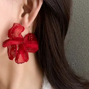 Detailed view of a large red fabric flower earring worn on an ear